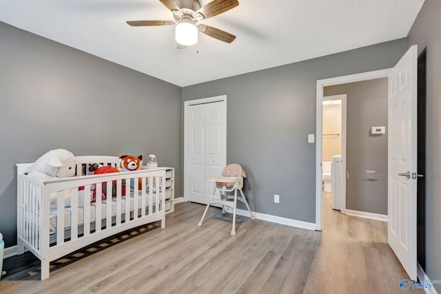 bedroom with a textured ceiling, a crib, baseboards, and wood finished floors