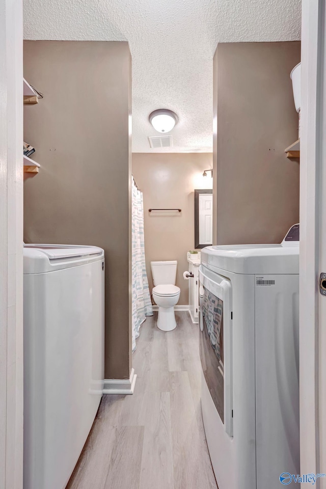 clothes washing area featuring laundry area, a textured ceiling, washer / clothes dryer, and wood finished floors