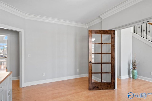 spare room featuring light wood-style floors, crown molding, baseboards, and stairs