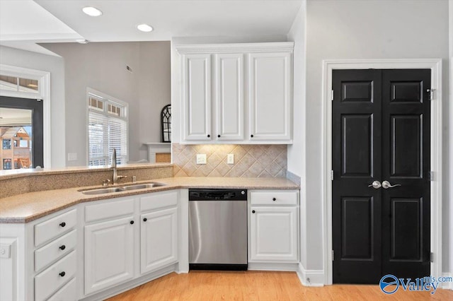 kitchen with tasteful backsplash, stainless steel dishwasher, white cabinets, a sink, and light wood-type flooring