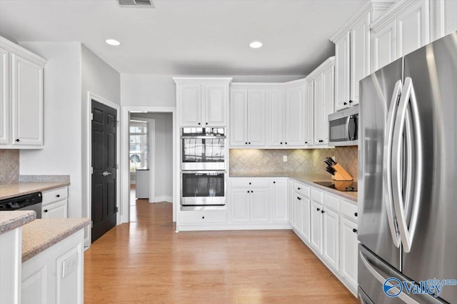 kitchen featuring light countertops, backsplash, appliances with stainless steel finishes, white cabinetry, and light wood-type flooring