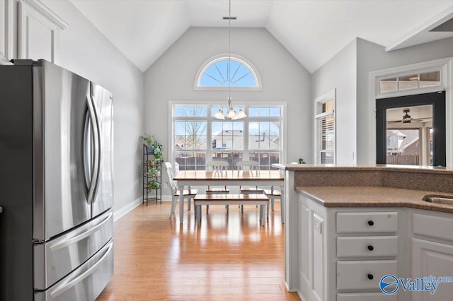 kitchen featuring a notable chandelier, light wood-style flooring, freestanding refrigerator, white cabinets, and vaulted ceiling