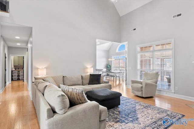 living room featuring high vaulted ceiling, visible vents, light wood-style flooring, and baseboards