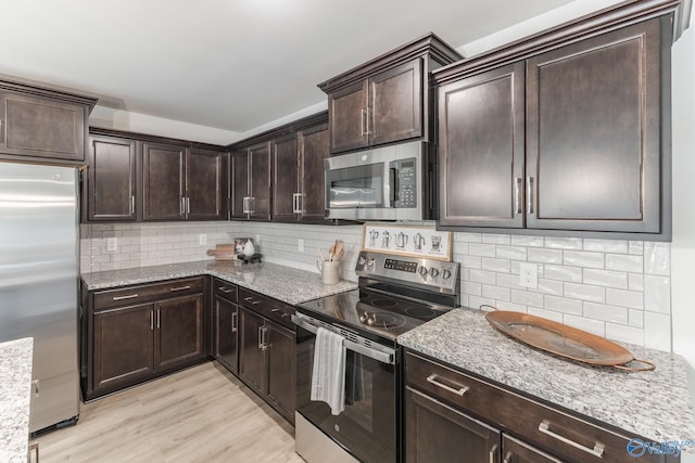 kitchen with stainless steel appliances, light stone counters, dark brown cabinetry, and light hardwood / wood-style flooring