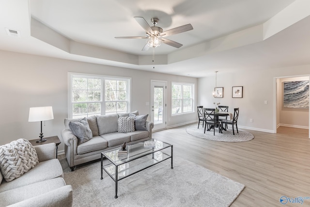 living room featuring a raised ceiling, ceiling fan, and light hardwood / wood-style floors