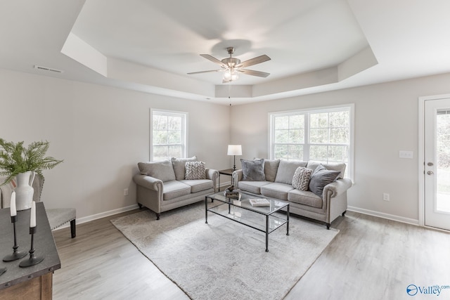 living room with a raised ceiling, ceiling fan, and light hardwood / wood-style floors