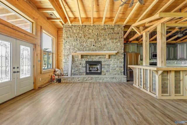 unfurnished living room with french doors, wooden ceiling, a stone fireplace, wood walls, and hardwood / wood-style flooring