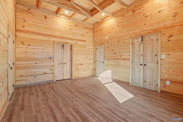 spare room with a towering ceiling, wooden walls, hardwood / wood-style floors, and beamed ceiling