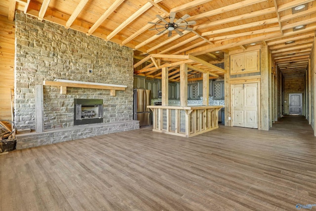 unfurnished living room featuring a stone fireplace, dark hardwood / wood-style floors, ceiling fan, beamed ceiling, and wood ceiling