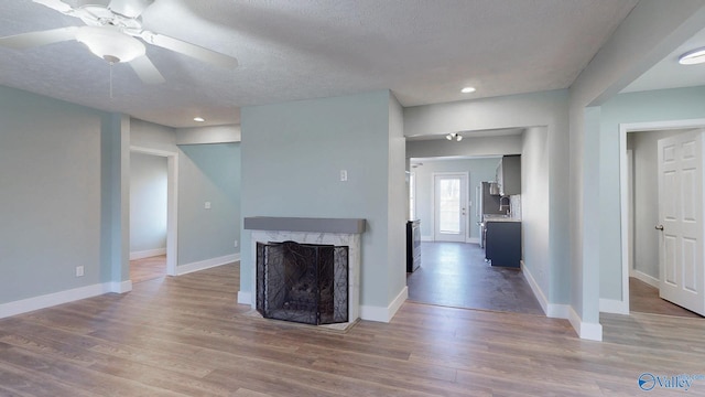 unfurnished living room featuring wood finished floors, baseboards, a high end fireplace, ceiling fan, and a textured ceiling