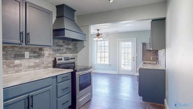 kitchen featuring backsplash, premium range hood, light countertops, stainless steel range with electric cooktop, and a sink