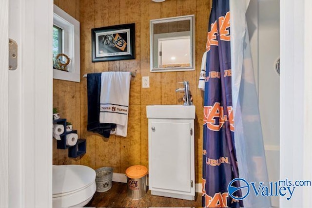 full bathroom with wood finished floors, wood walls, a sink, and toilet