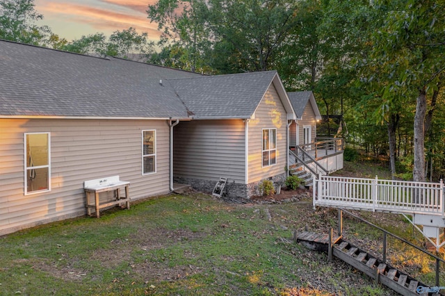 back of property at dusk featuring a shingled roof, a deck, and a yard