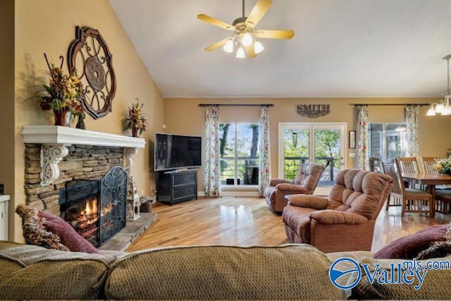 living room with ceiling fan with notable chandelier, a fireplace, lofted ceiling, and wood finished floors