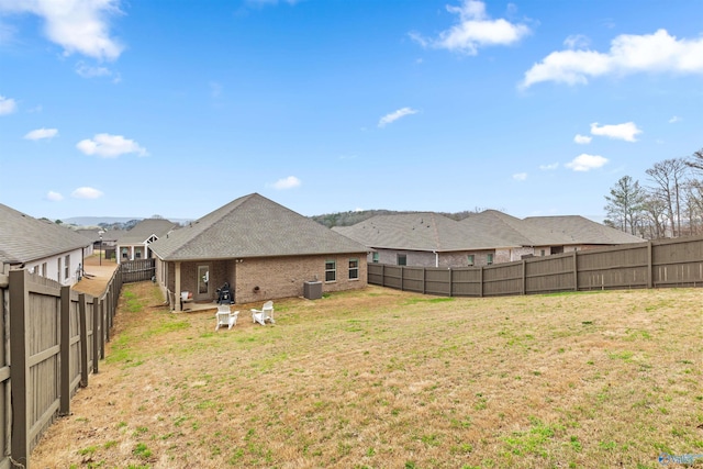 back of house featuring a yard, brick siding, central AC, and a fenced backyard