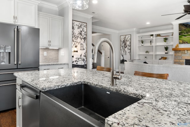 kitchen with a ceiling fan, high quality fridge, ornamental molding, light stone counters, and a sink