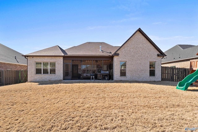 rear view of house with a playground, brick siding, roof with shingles, a patio area, and a fenced backyard