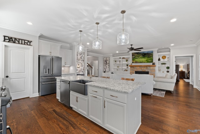 kitchen featuring crown molding, appliances with stainless steel finishes, dark wood-type flooring, a kitchen island with sink, and a sink