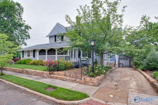 view of front of property featuring covered porch, driveway, roof with shingles, and a detached garage