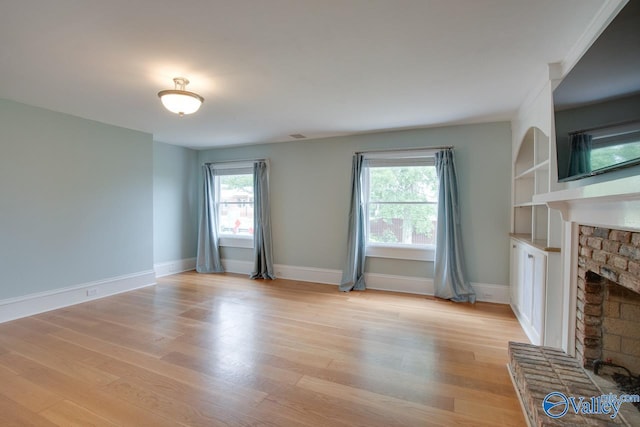 717 NE Eustis Ave, Huntsville, AL 35801 - unfurnished living room featuring a brick fireplace, light wood-style floors, baseboards, and built in shelves