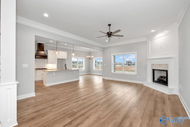 unfurnished living room featuring light wood finished floors, ornamental molding, a fireplace with raised hearth, and ceiling fan with notable chandelier