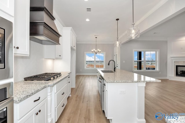 kitchen featuring stainless steel appliances, white cabinets, a sink, an island with sink, and light stone countertops