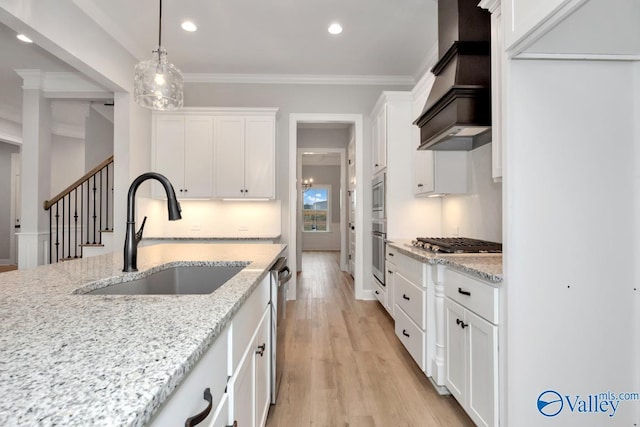 kitchen featuring light stone countertops, premium range hood, white cabinets, and a sink