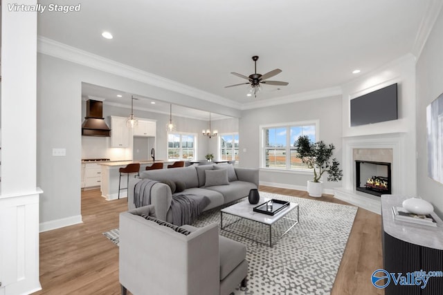 living area featuring a wealth of natural light, a high end fireplace, crown molding, and light wood-style flooring