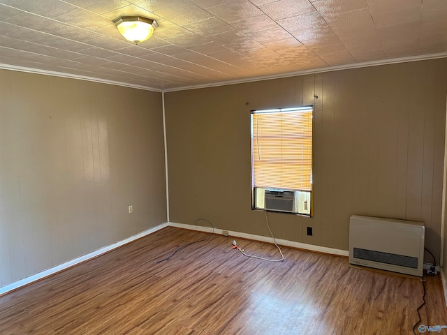 empty room with heating unit, crown molding, wooden walls, and wood-type flooring