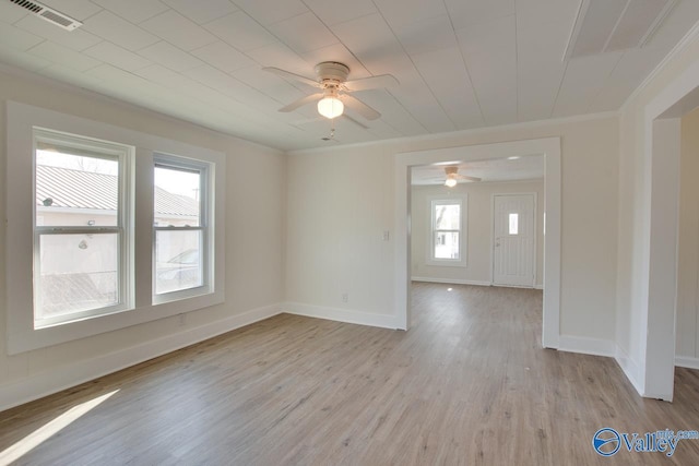 empty room with crown molding, a ceiling fan, light wood-style flooring, baseboards, and visible vents