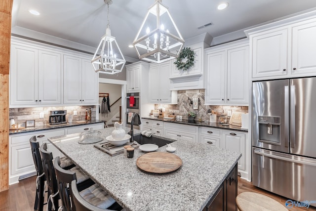 kitchen featuring stainless steel refrigerator with ice dispenser, white cabinets, decorative light fixtures, a center island with sink, and a chandelier