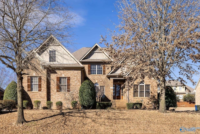 view of front of home with a shingled roof, brick siding, and fence