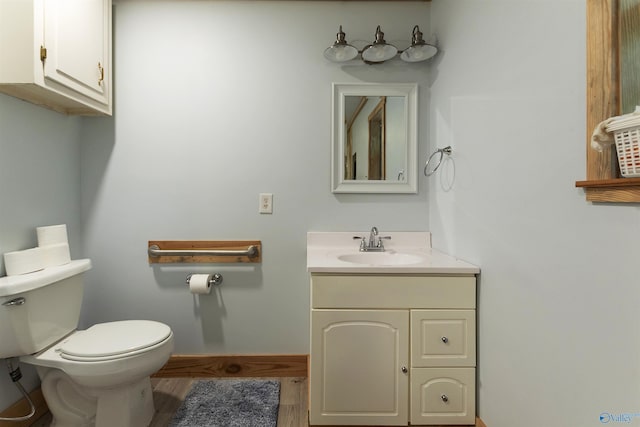 bathroom featuring toilet, baseboards, wood finished floors, and vanity