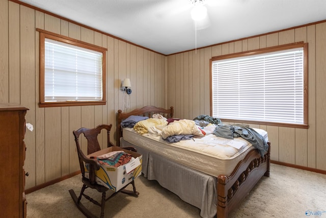 bedroom with baseboards, wood walls, light carpet, and multiple windows
