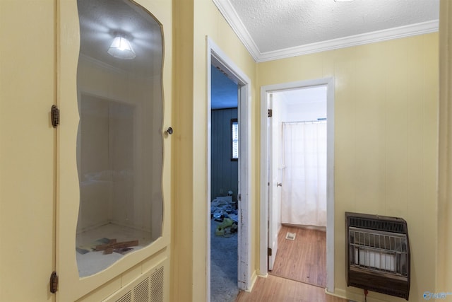 hall featuring heating unit, a textured ceiling, ornamental molding, and wood finished floors