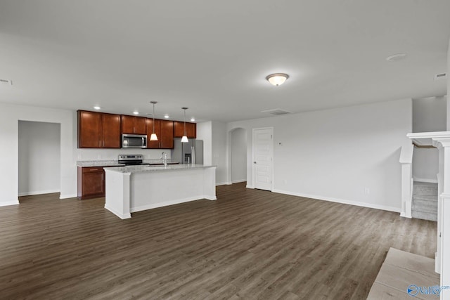 kitchen featuring appliances with stainless steel finishes, an island with sink, dark hardwood / wood-style flooring, decorative light fixtures, and sink