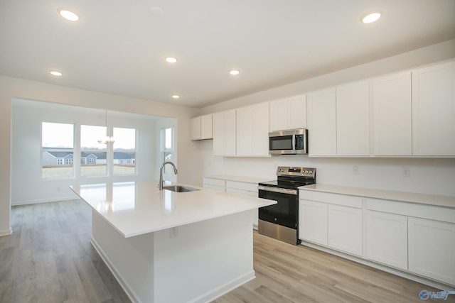 kitchen featuring stainless steel appliances, sink, white cabinetry, light wood-type flooring, and a kitchen island with sink