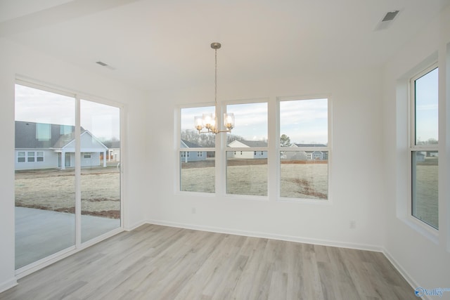 unfurnished dining area with light wood-type flooring, a healthy amount of sunlight, and a notable chandelier