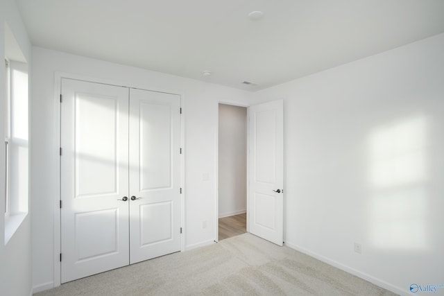 unfurnished bedroom with light colored carpet and a closet