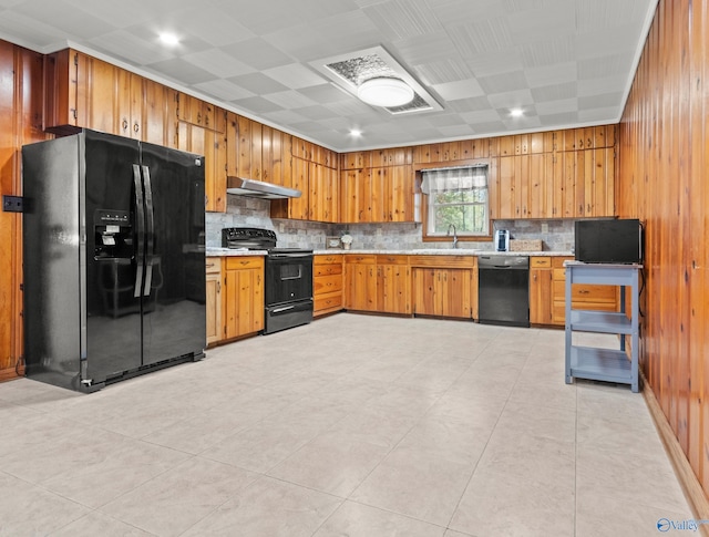 kitchen featuring sink, backsplash, wooden walls, light tile patterned floors, and black appliances