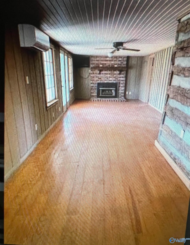 unfurnished living room with wood walls, ceiling fan, carpet, and a brick fireplace