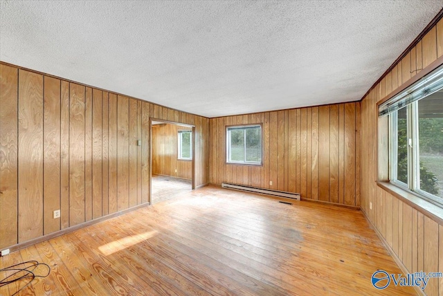 spare room with plenty of natural light, a baseboard heating unit, a textured ceiling, and light hardwood / wood-style floors