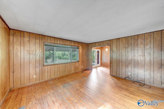 unfurnished room with light hardwood / wood-style floors, a textured ceiling, and wood walls