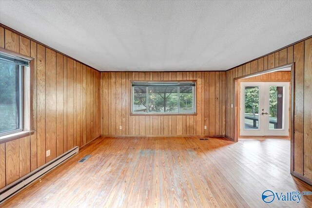 spare room featuring french doors, a baseboard radiator, light hardwood / wood-style flooring, and a wealth of natural light