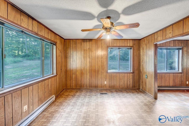 empty room featuring a baseboard radiator, a wealth of natural light, and wood walls