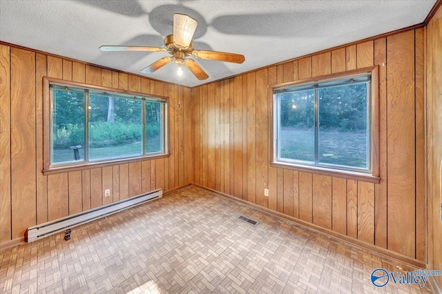 empty room featuring a baseboard heating unit, a wealth of natural light, a textured ceiling, and wood walls