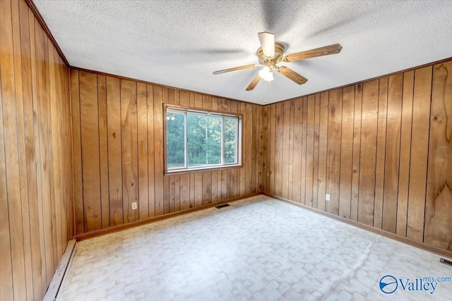 spare room with baseboard heating, ceiling fan, a textured ceiling, and wood walls