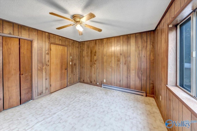 empty room featuring ceiling fan, a baseboard radiator, wooden walls, and a textured ceiling