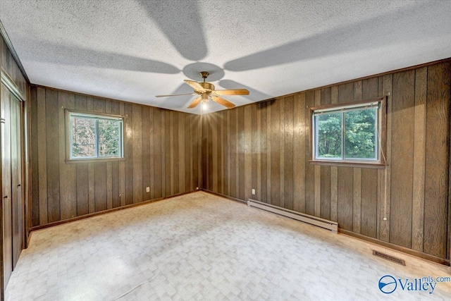 spare room featuring a textured ceiling, a baseboard radiator, wooden walls, and ceiling fan