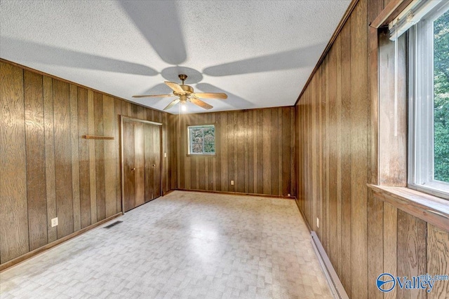 unfurnished room featuring ceiling fan, a baseboard heating unit, a textured ceiling, and wood walls